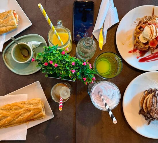 Mesa de desayuno con tostadas, zumos y gofres en Elzade Cafe